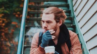 階段でコーヒーを飲みながらタバコを吸う男性